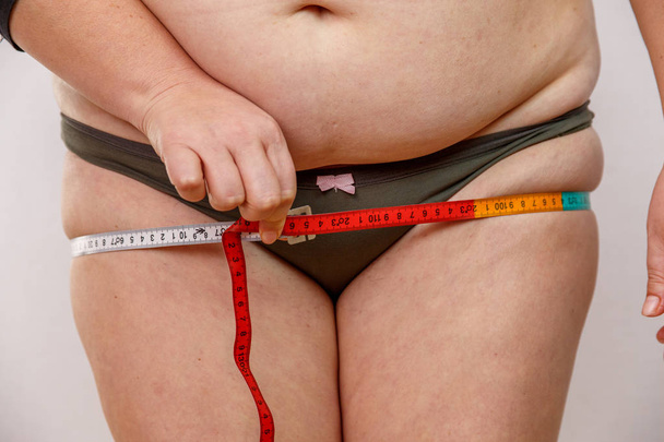 une femme d'âge moyen avec un surpoids en sous-vêtements mesurant son corps
 - Photo, image