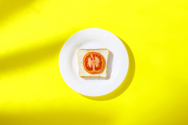 Sandwich con tomate sobre un plato blanco sobre fondo amarillo. Concepto de desayuno saludable, vitaminas, dieta, pérdida de peso. Piso tendido, Vista superior
 - Foto, Imagen