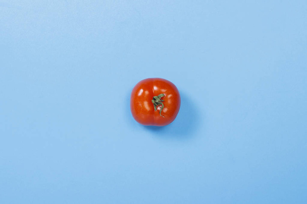 Tomaatti sinisellä pohjalla. Vitamiinien käsite, kesäaika, aamiainen. Tasainen, ylhäältä
. - Valokuva, kuva
