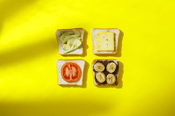 Sandwiches mit Banane, Tomate, Avocado, Blauschimmelkäse auf gelbem Hintergrund. Konzept eines gesunden Frühstücks, Vitamine, richtige Ernährung. natürliches Licht, Schatten von Pflanzen. flache Lage, Draufsicht. - Foto, Bild