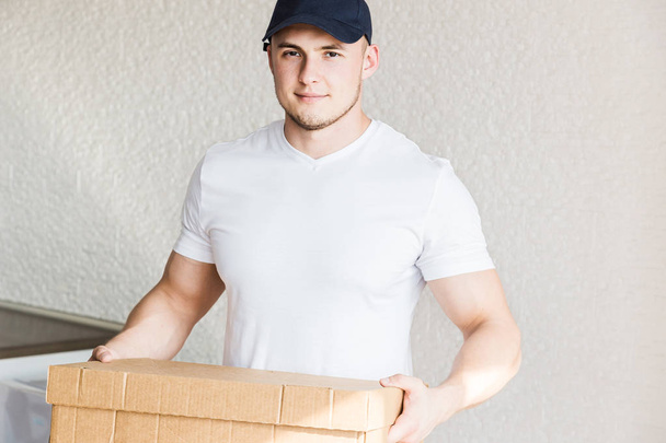 Delivery strong, muscular man loading cardboard boxes for moving to an apartment. professional worker of transportation, male loaders in overalls. free space for text, isolated - Фото, изображение