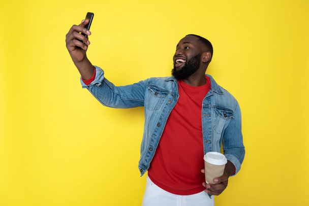 カップホルダーとスマートフォンを腕に抱きしめる笑顔のアフリカ人男性のウエストアップ - 写真・画像