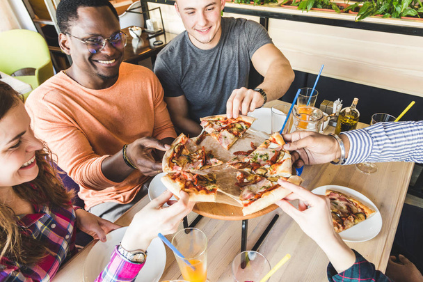 Společnost multikulturních mladých lidí v kavárně, kteří jedí pizzu, pijí koktejly, baví se - Fotografie, Obrázek