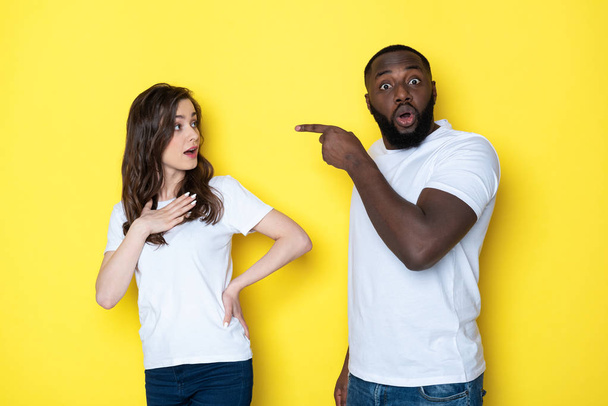 Stressed young interracial couple in white T-shirts posing for camera in studio - Фото, изображение