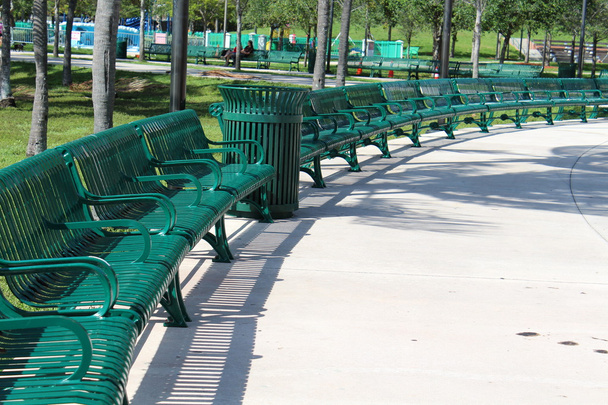 Чистый и упорядоченный полукруг расположения зеленых металлических скамеек в парке
 - Фото, изображение