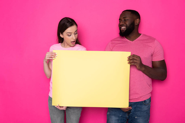 Young interracial couple holding empty yellow banner with copy space in studio - Фото, зображення