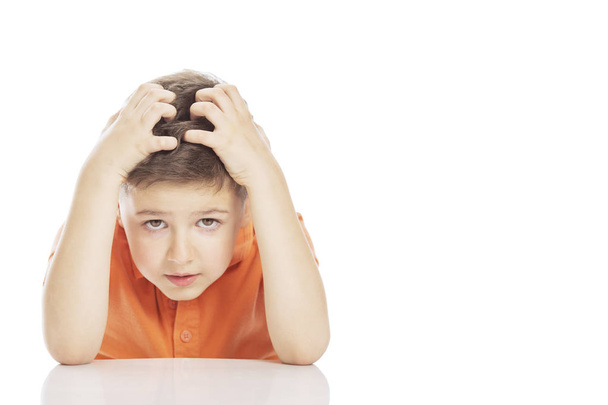 The boy is sitting at the table, holding his head with his hands. Close-up. Isolated on a white background. - Photo, image
