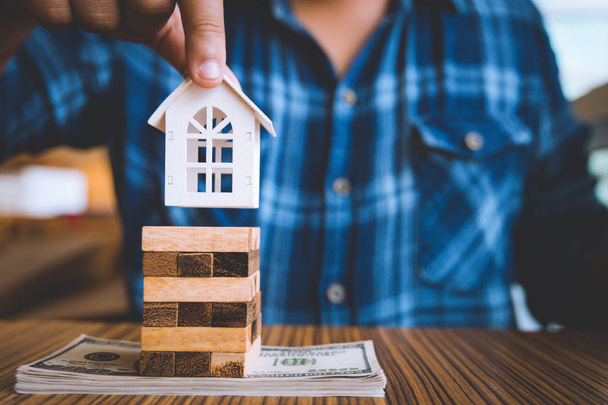 Hand holding a piece of wood block with model white house on dollar banknote. Insurance and property investment real estate concept. - Photo, Image