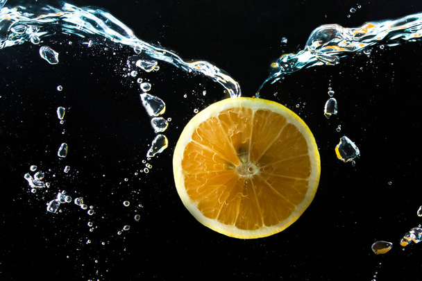 Rebanada de naranja en salpicadura de agua en negro
 - Foto, imagen