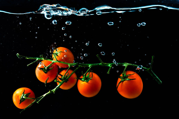 Червоні вишневі помідори під водою з бульбашками на чорному
 - Фото, зображення