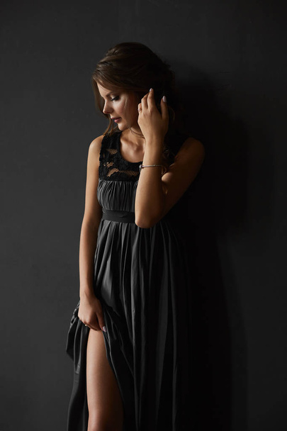 ファッショナブルなイブニングドレスで完璧なボディを持つセクシーなブルネットの美しさは、暗い背景で彼女の長いセクシーな脚をバール - 写真・画像