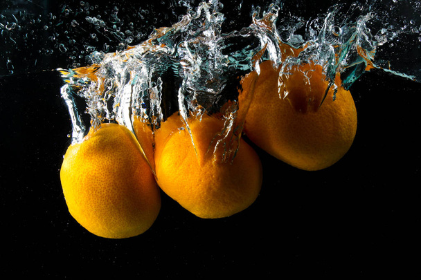 Τρία ώριμα πορτοκαλί στο νερό που πιτσιλίζουν στο μαύρο - Φωτογραφία, εικόνα