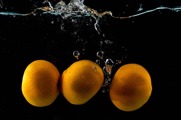 Three ripe clementine in water splash on black - Foto, imagen