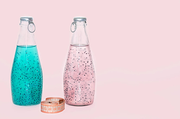 A centimeter and glass bottles with blue and pink basil seed stand on a pink background. - Photo, Image