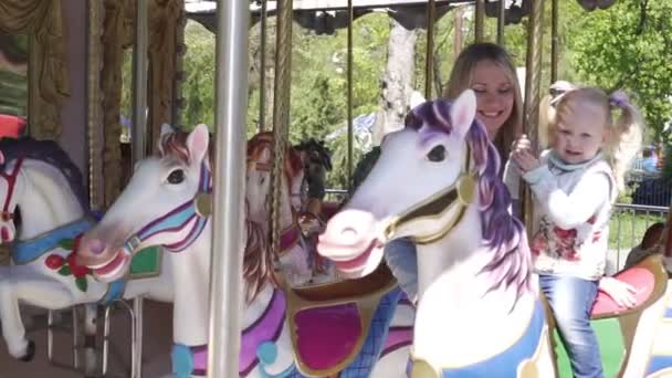 Een klein kind rijdt op een paarden carrousel. - Video