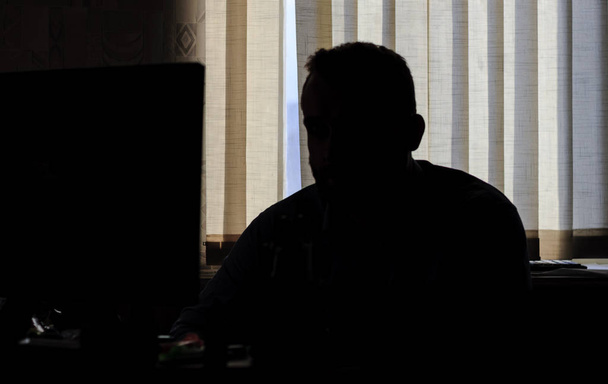 L'uomo si siede in ufficio al computer. solo silhouette. Guarda le telecamere sul monitor.
. - Foto, immagini