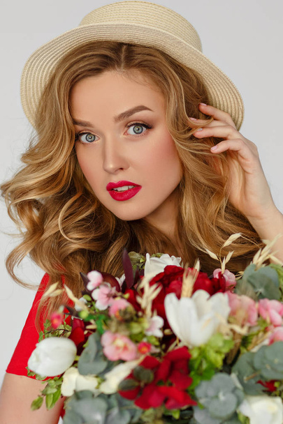 Beautiful girl blonde in a hat and a red blouse holding flowers  - 写真・画像