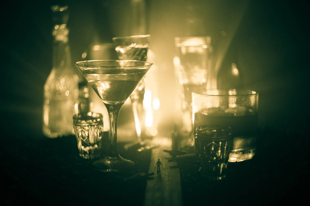 Абстрактная концепция алкоголизма. Силуэт мужчины, стоящего посреди дороги в туманную ночь в огромных стаканах, наполненных алкогольными напитками. Творческое оформление произведений искусства
 - Фото, изображение