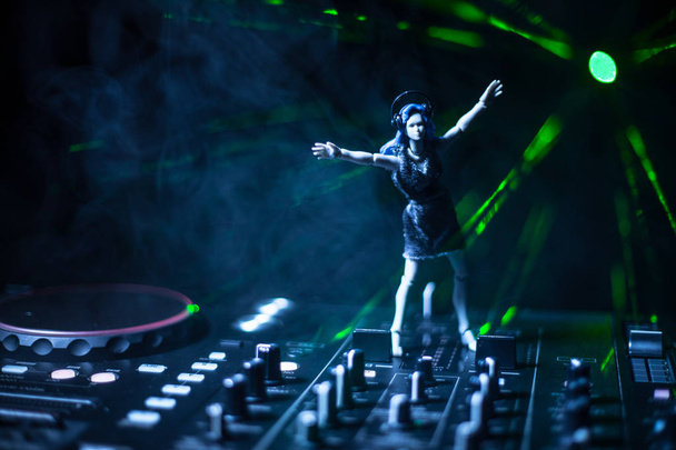 Concept de club DJ. Femme DJ mélange, et Scratching dans une boîte de nuit. Silhouette de fille sur le pont de DJ, lumières stroboscopiques et brouillard sur le fond. Décoration artistique créative avec jouet. Concentration sélective
 - Photo, image