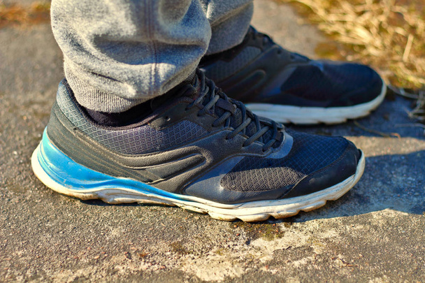 Sağlıklı ve aktif spor yaşam tarzları için asfalt konsepti üzerinde beyaz ve mavi tabanlı gri eşofmanlı bacaklar ve siyah koşu ayakkabıları - Fotoğraf, Görsel