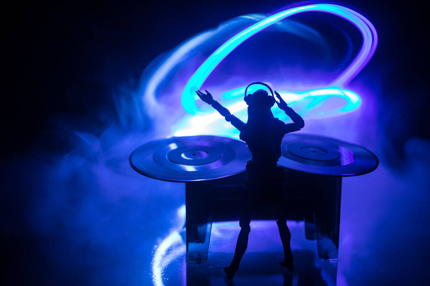 Dj club concept. Woman DJ mixing, and Scratching in a Night Club. Girl silhouette on dj's deck, strobe lights and fog on background. Creative artwork decoration with toy. Selective focus - Photo, Image