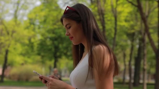 Lezende vrouw in smartphone wandelen in het zomerpark - Video