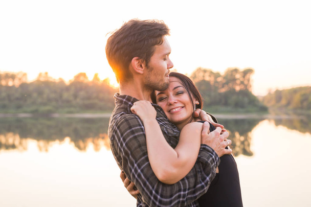 Relationship, love and nature concept - Close up portrait of attractive woman and handsome man hugging on the background of the lake - Photo, Image