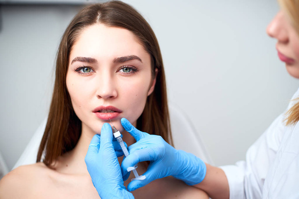 Lip Augmentation. Closeup Of Beautician Doctor Hands Doing Beauty Procedure To Female Lips with Syringe. Young Womans Mouth Receiving Hyaluronic Acid Injection. Cosmetology Treatment. Mesotherapy. - Φωτογραφία, εικόνα