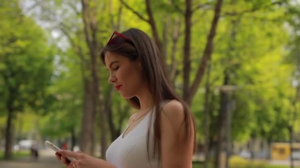 Woman reading message in smartphone walking at summer park - Filmati, video