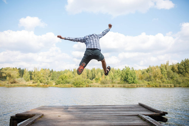 Obraz z tyłu skaczący człowiek na drewnianym moście przez rzekę - Zdjęcie, obraz