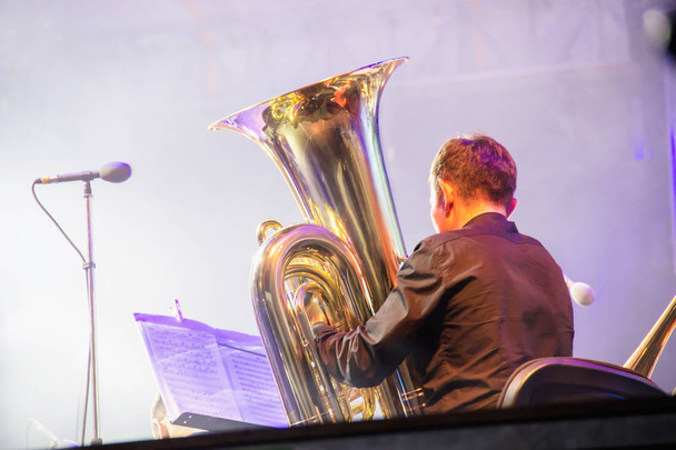 Παίκτης τούμπα σε μια ορχήστρα στη σκηνή, παίζει σε μεγάλο μπρούτζινο σωλήνα, πίσω από τα παρασκήνια γυρίσματα - Φωτογραφία, εικόνα