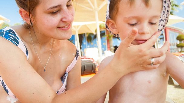 Close-up foto de yougn mãe com seu filho criança usando protetor solar loção na praia do mar
 - Foto, Imagem