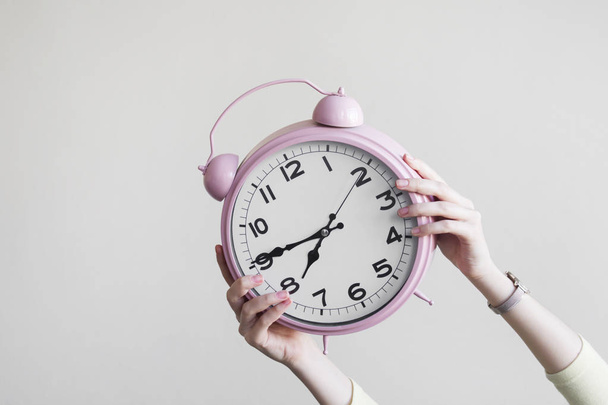 Woman holding alarm clock in one hand on gray background - Photo, Image