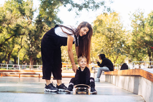 Jonge moeder leert haar kleine jongen op een skateboard te rijden - Foto, afbeelding