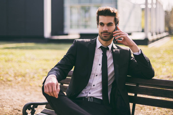 Elegant businessman using phone while sitting outdoor.Toned image. - Foto, Imagen