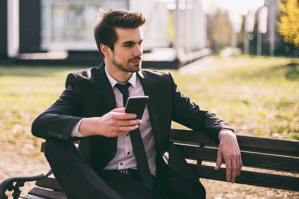 Elegant businessman using phone while sitting outdoor.Toned image. - Foto, Bild