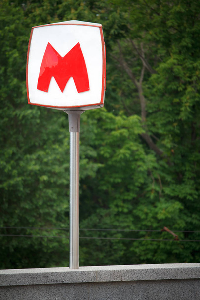 De grote rode letter M geeft de toegang tot de ondergrondse metro tegen de achtergrond van een groen park - Foto, afbeelding