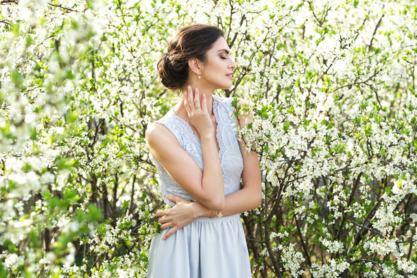 Mujer hermosa y delicada en vestido largo rodeada de árboles florecientes
. - Foto, imagen