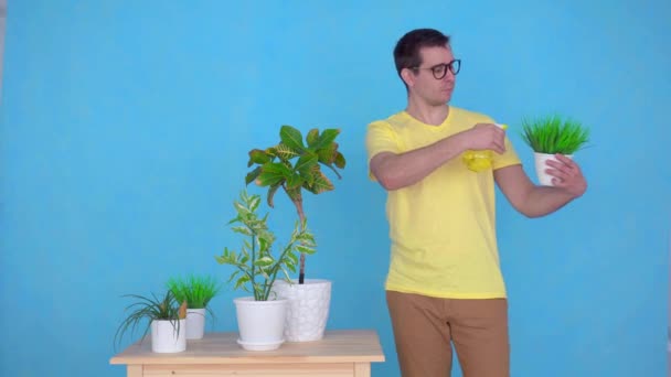 man with glasses sprays plants on the table at home,looking at the camera smiling - Video
