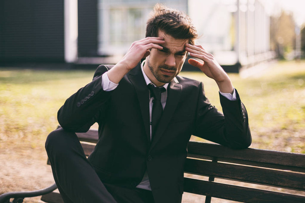 Elegant businessman having a headache while sitting outdoor.Toned image. - Foto, afbeelding