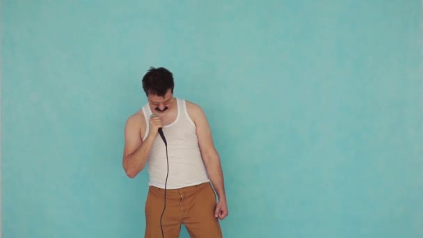 Αστείος νέος άντρας σε γυαλιά με μικρόφωνο στο χέρι σε μπλε φόντο αργή mo - Πλάνα, βίντεο