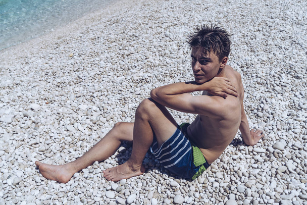 portret młodego mężczyzny siedzi przy kamienistej plaży - Zdjęcie, obraz