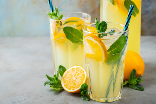 レモンとミントの入ったレモネードやモヒートカクテル、素朴な青を背景に氷と冷たいさわやかな飲み物や飲み物を備えた2つのガラス。スペースのコピー - 写真・画像