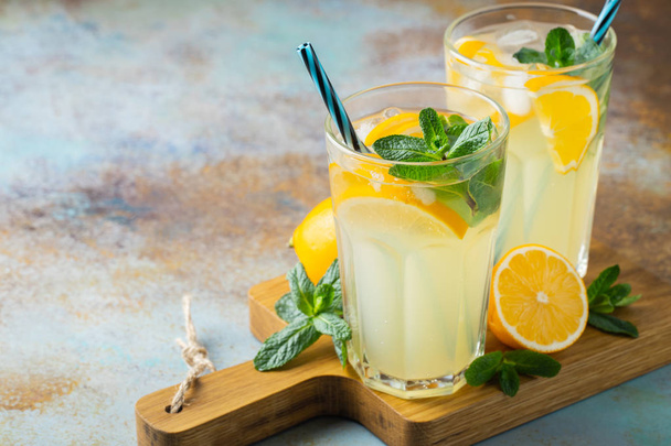 Two glass with lemonade or mojito cocktail with lemon and mint, cold refreshing drink or beverage with ice on rustic blue background. Copy space - Foto, Imagem