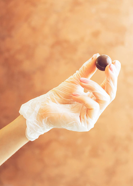 Main gantée féminine tenant un bonbon au chocolat rond. Fabrication de chocolats faits à la main. Minimalisme. Cadre vertical
. - Photo, image