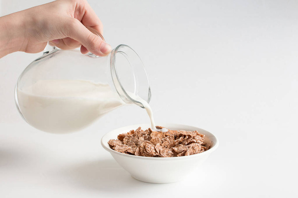 Nalewanie mleka do miski z wieloziarnistego naturalnego płatków na białym tle. Zdrowa żywność.  - Zdjęcie, obraz