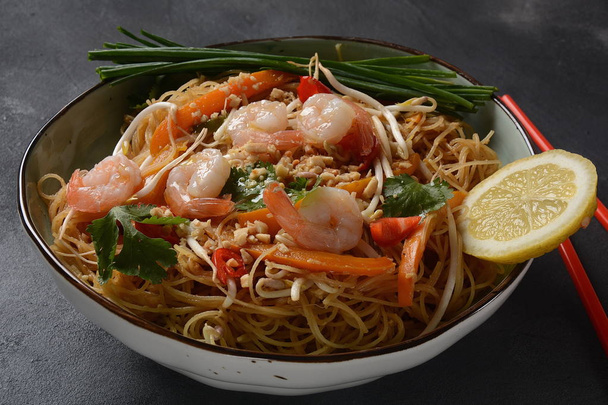 Pad Thai- traditional Thai dish with stir fried rice noodles, shrimps and vegetables on a dark background, copy space - Photo, image