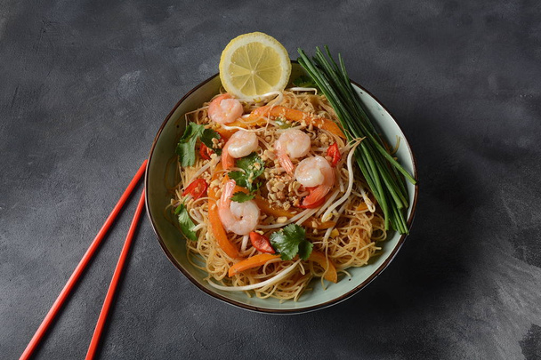 Pad Thai- traditional Thai dish with stir fried rice noodles, shrimps and vegetables on a dark background, copy space - Foto, Bild