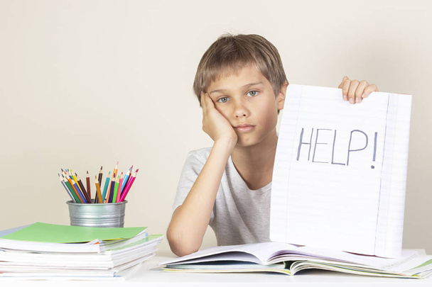 Aide à signer. Triste fatigué malheureux enfant faire ses devoirs et tenant un carnet avec mot Aide
 - Photo, image