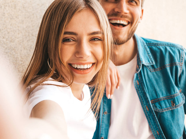 Smiling beautiful girl and her handsome boyfriend in casual summer clothes. Happy family taking selfie self portrait of themselves on smartphone camera. Having fun on the street background  - Fotografie, Obrázek